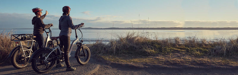 Two riders stand on their ebikes next to an ocean bluff.