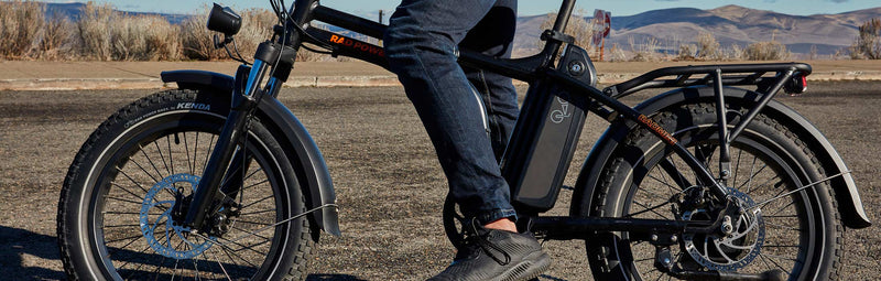 A man stands over his RadMini folding bike on a rural highway.