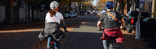 A man and a woman ride electric bikes while wearing Rad Power Bikes X Pabst Blue Ribbon gear.