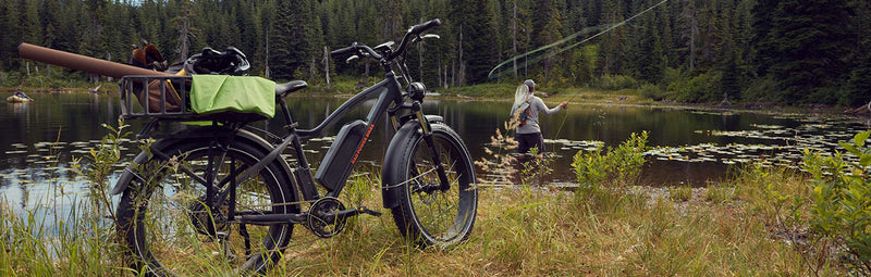 A RadRover in the foreground by a woodsy lake. A fisherman is in the background.