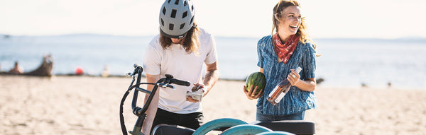 A woman and man unload wine and a watermelon from their RadRunner at the beach