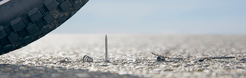 A bike tire about to run over a screw on the ground. 