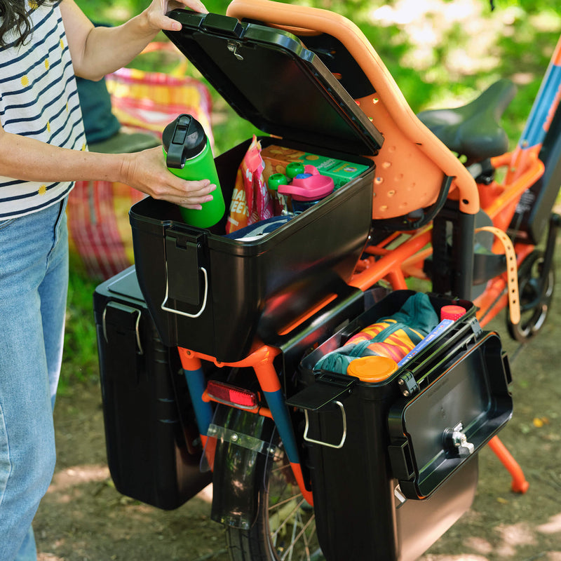 Woman loading gear into a Rad hardshell locking box, featured along with two panniers on a RadWagon electric cargo bike.