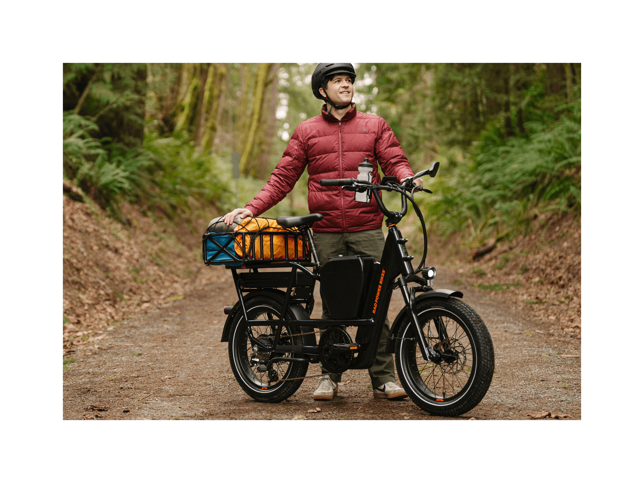 A man wearing a black bicycle helmet wearing a red jacket standing next to a green ebike with a rear basket and mirror.