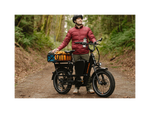 A man wearing a black bicycle helmet wearing a red jacket standing next to a green ebike with a rear basket and mirror.