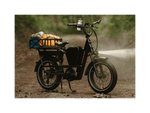 A emerald green ebike resting on its kickstand on a trail in a forest.