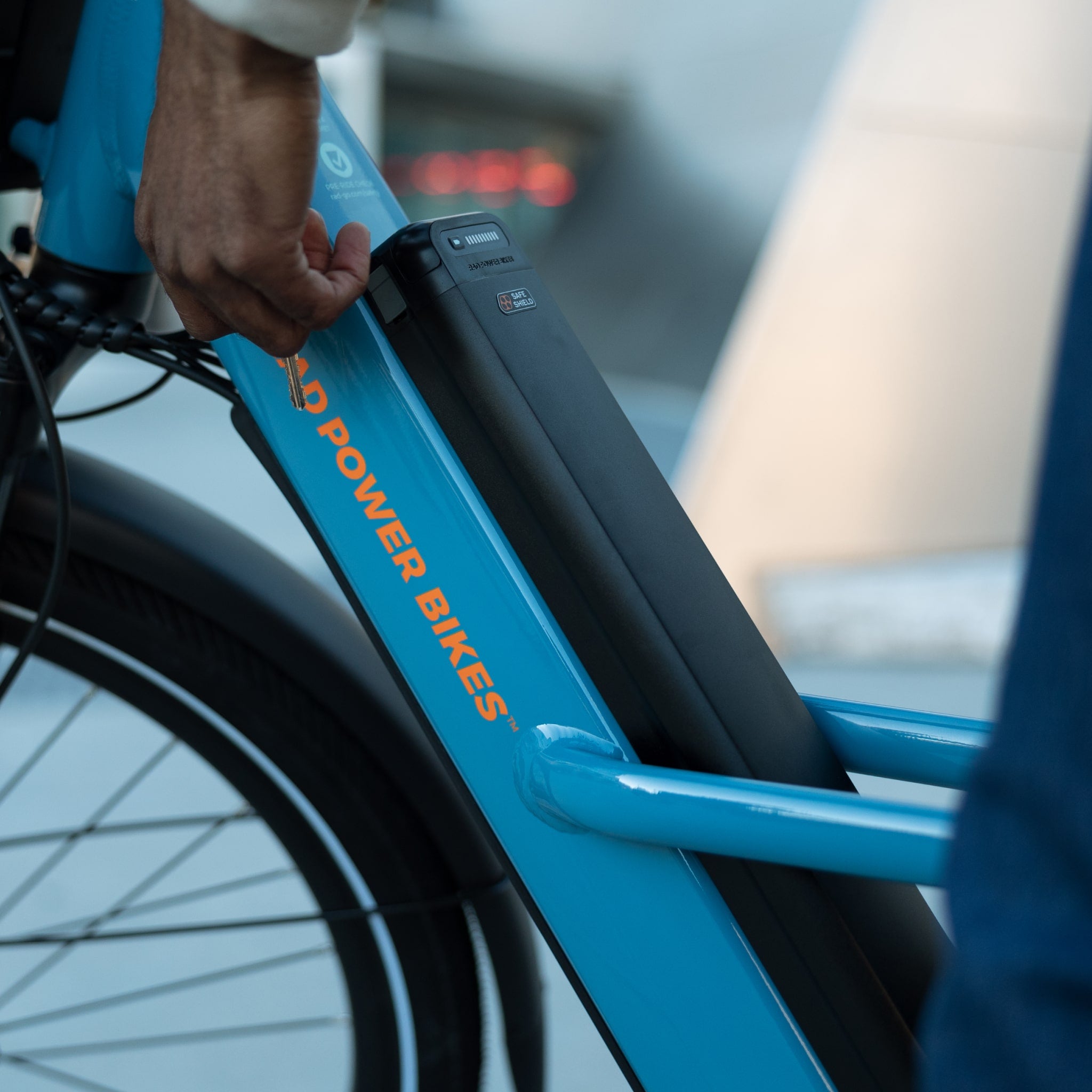Person managing the key for a Safe Shield Advanced Semi-Integrated battery installed on a blue Radster Road electric commuter bike