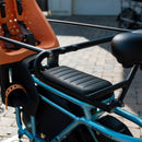 Man riding a blue RadWagon 5 electric cargo bike with two children as passengers. The children are seated with passenger accessories including the RadWagon 5 Deckpad, an orange thule yepp child seat and a caboose.